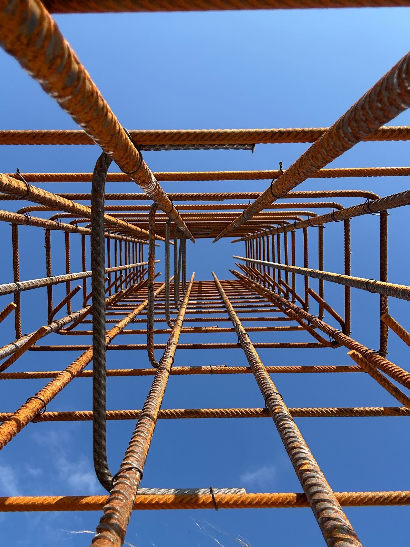 A tied steel rebar cage for a foundation column, photographed looking up against a blue sky